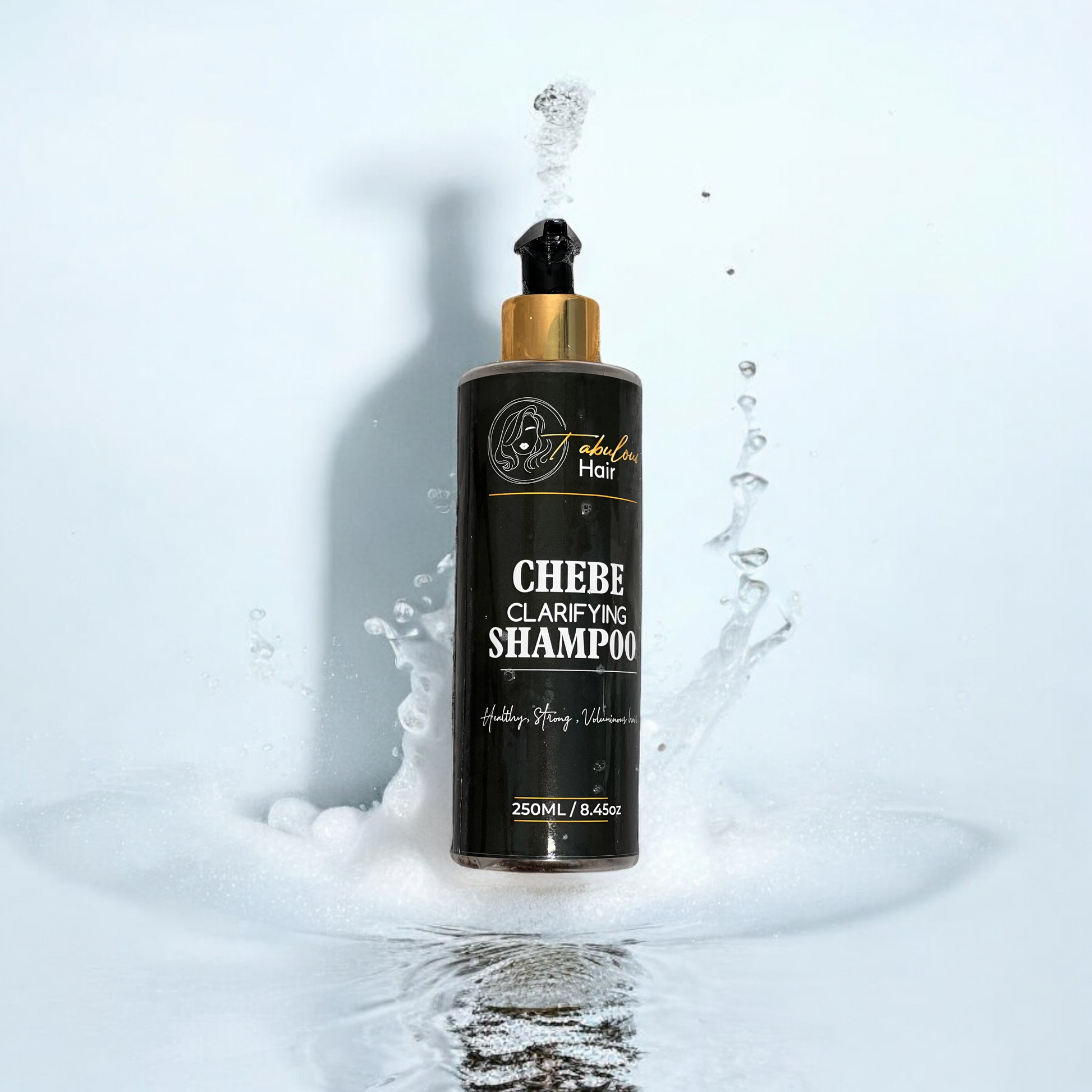 A bottle of Chebe Clarifying Shampoo floating in clear water. The sleek black and gold bottle features bold white text displaying the product name and its benefits: "Healthy, Strong, Voluminous Hair." The shampoo is designed to deeply cleanse, remove buildup, and promote hair health. The water background emphasises the refreshing, clarifying nature of the product.