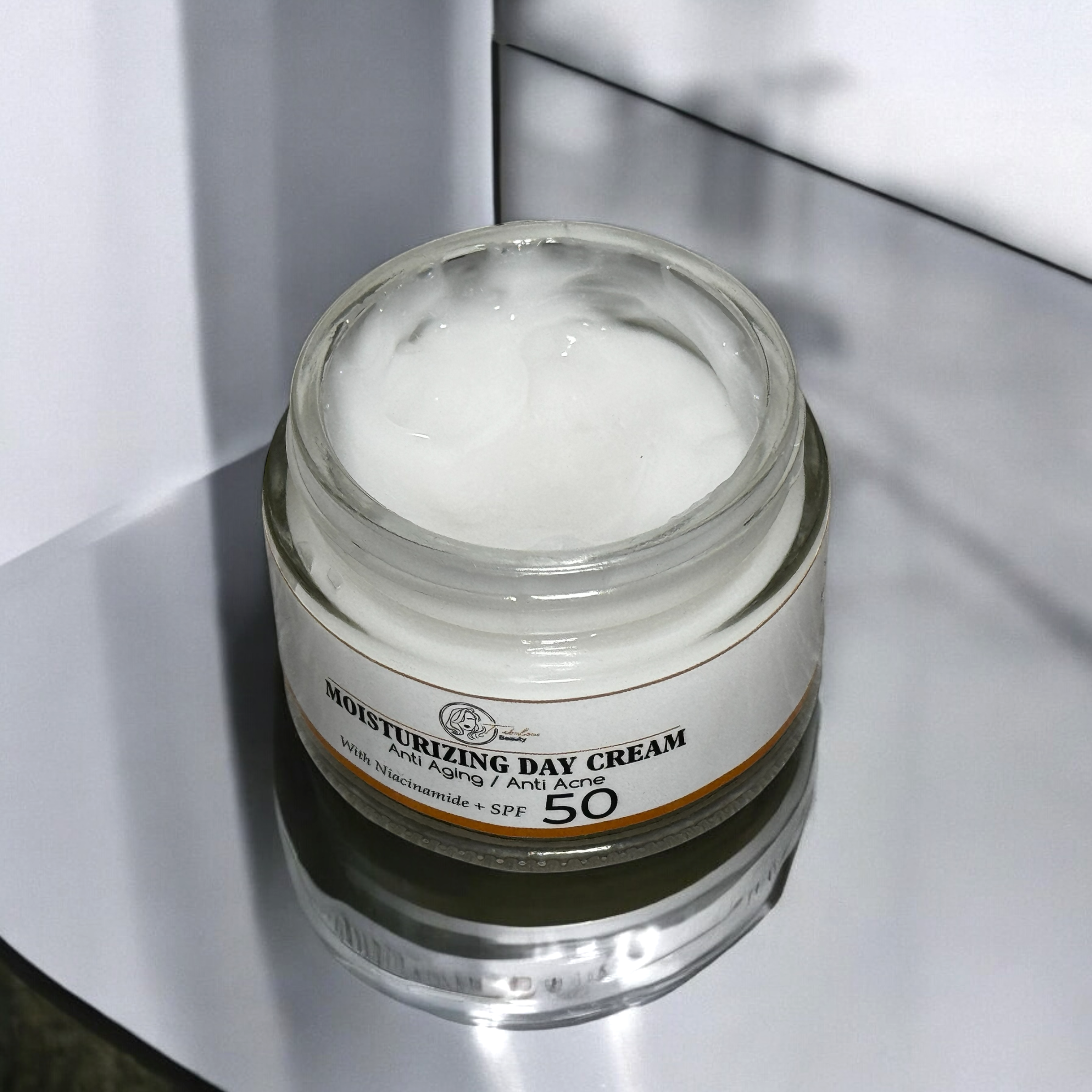 A jar of Moisturising Day Cream sits open, showcasing its smooth, creamy texture. The label highlights its anti-aging and anti-acne benefits with SPF 50 protection, making it ideal for daily skincare. The jar is placed on a reflective surface, giving the product an elegant and luxurious feel