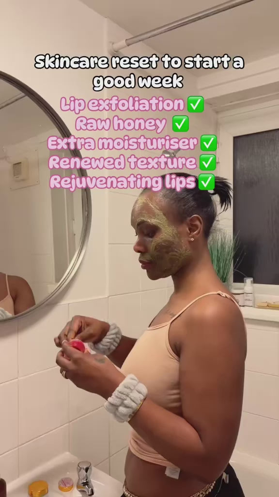 Load video: A young lady gently exfoliates her lips with a strawberry lip scrub. She rubs the scrub in circular motions, smiling as the sugary texture buffs away dead skin. The bright red strawberry scrub gives her lips a light tint, while the scene captures her enjoying the sweet scent and refreshing feel. Her lips look smooth and moisturized as she wipes away the scrub, leaving a soft, natural glow